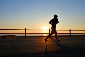 The silhouette of a male runner jogger running on beach boardwalk next to ocean at sunrise or sunset